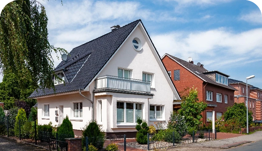 Weißes Einfamilienhaus mit dunklem Dach und Balkon an einer Wohnstraße