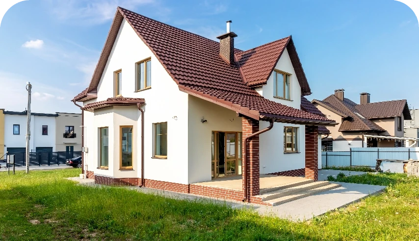 Weiß gestrichenes Einfamilienhaus mit braunem Ziegeldach, davor ein Rasen