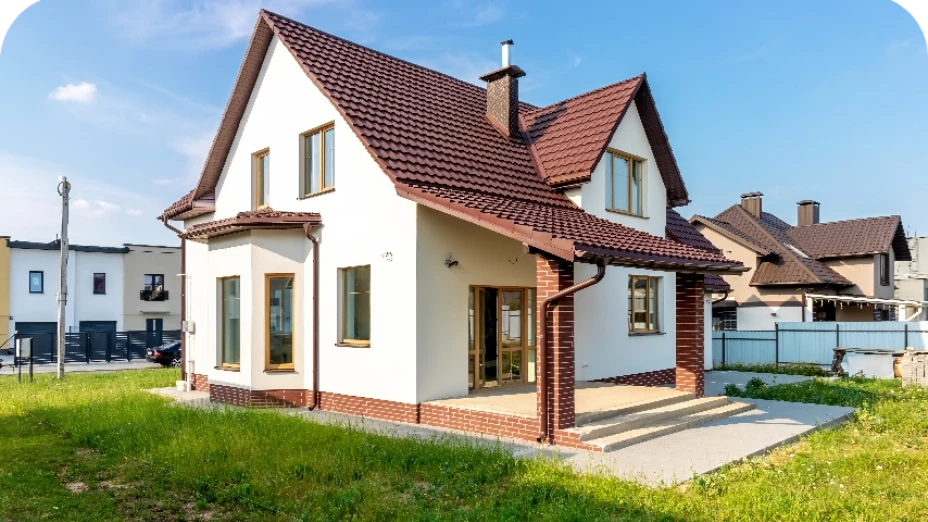 Weiß gestrichenes Einfamilienhaus mit braunem Ziegeldach, davor ein Rasen