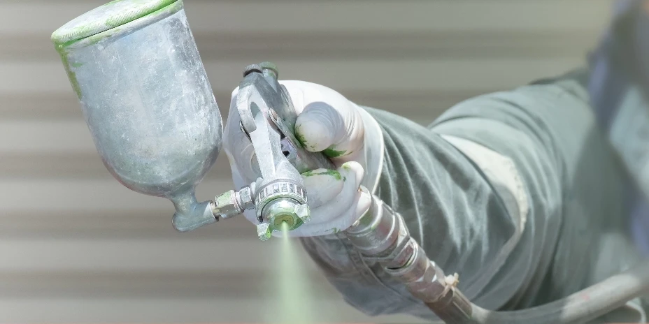 Handwerker lackiert eine Metallfläche mit einer Spritzpistole